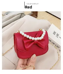 Detail of red mini crossbody bag with a large bow, pearl handle, and gold chain strap