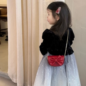 Detail of red bow kids crossbody bag with golden chain strap on model in velvet dress