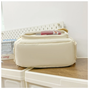 Detail view of cream toddler backpack featuring a clear PVC window with a smiley bag inside