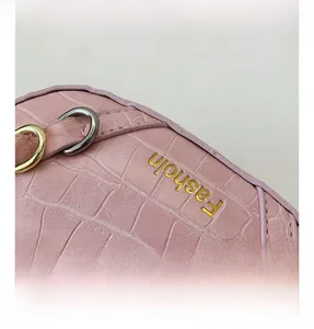 Dettaglio della trama in pelle di coccodrillo rosa con anello a D dorato e logo inciso