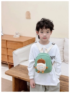 Toddler green canvas backpack with plush acorn decoration worn by a child in home setting