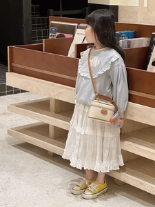Toddler girl in light blue ruffled sweatshirt and white tiered skirt with mini box bag