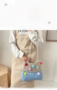 Close-up of handmade crochet shoulder bag with colorful pom-poms and hollow mesh texture