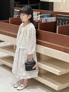 Detail of a white lace cardigan paired with a floral dress and a mini black leather handbag