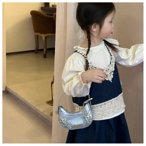 Dettaglio della borsa a mezzaluna argentata con trama coccodrillo indossata da bambina
