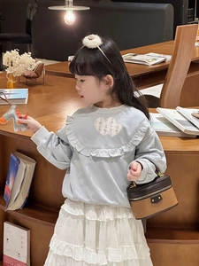 Close-up of heart pattern embroidery and ruffled lace detail on girls' sweatshirt