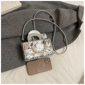 Detailed macro view of a silver sequined mini handbag with elegant pearl handle and metal rings