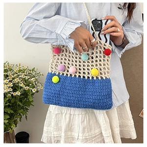 Detail of a handmade crochet tote bag featuring colorful pompoms and a dual-tone weave