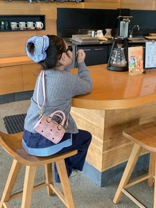Close-up of pink mini bear-print Boston bag worn by a child in a cafe setting