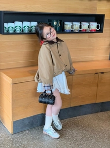 Detail of child wearing khaki jacket with corduroy collar and plaid cuffs holding bag