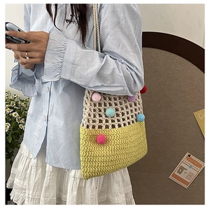 Detail of hand-crocheted hollow shoulder bag with colorful pom-poms and yellow base