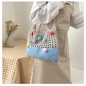 Detail of hand-woven hollow knit tote bag with colorful pom-poms and two-tone stitching