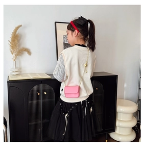 Pink mini crossbody bag for kids with gold chain strap shown on model in cozy home setting
