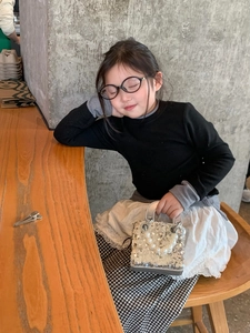 Detail of silver sequin mini handbag with pearl handle held by a child at a table