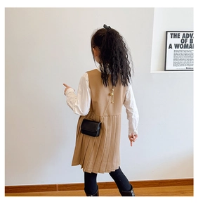 Rear view of a girl wearing a black mini crossbody chain bag and brown pleated school dress