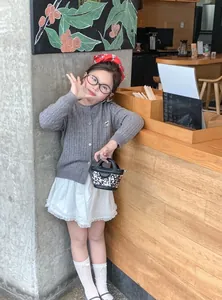 Fille en cardigan gris et jupe en dentelle avec mini sac imprimé dans un café chaleureux