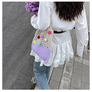 Detail view of handmade crochet shoulder bag with colorful pom-poms and purple hollow design