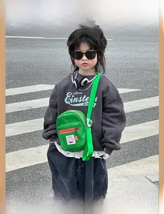Close-up of bright green kids' nylon crossbody bag with orange zipper and cartoon patch