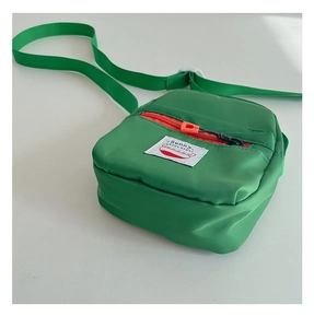 Detail view of green nylon kids crossbody bag with orange zipper and sunny kids label