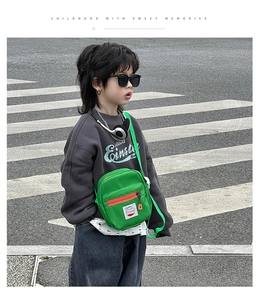 Close-up of bright green kids mini crossbody bag with red zipper and letter patch