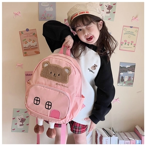Pink cartoon bear backpack with plush 3D legs shown on a young girl in a warm setting