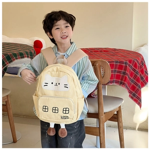 Dettaglio del ricamo di gatto e ciondoli di peluche su zaino in tela beige per bimbi