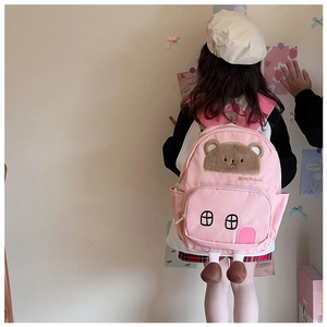 Pink house-shaped toddler backpack with plush bear detail shown on child model