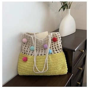 Close-up of crochet tote bag with colorful pom-poms on a rustic wooden cabinet
