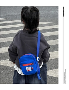 Rear view of a child wearing a royal blue nylon crossbody bag with red zippers and strap