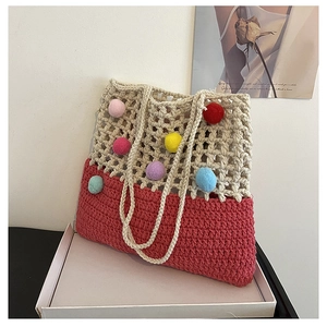 Detail of a handmade crochet tote bag featuring vibrant colorful pom-poms and red base