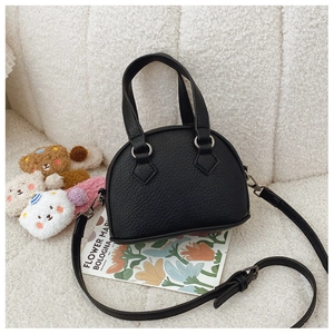 Detail of black mini shell bag with lychee texture and adjustable strap on soft background
