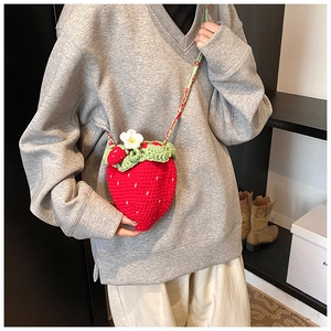 Detail of a handmade crochet strawberry crossbody bag with green leaf and flower details