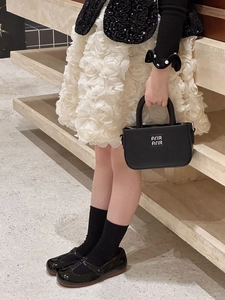 Détail d'un mini sac à main noir en cuir pour enfants avec poignées et logo blanc