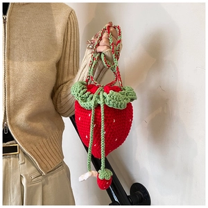 Detail of handmade crochet strawberry bag featuring red yarn seeds and green leaf closure