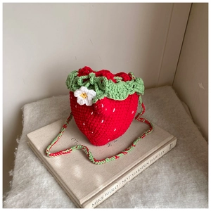 Detailed macro view of handmade crochet strawberry bag with green leaves and a small white flower