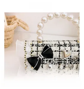 Close-up of black and white tweed bag with faux pearl handle and metal heart charm