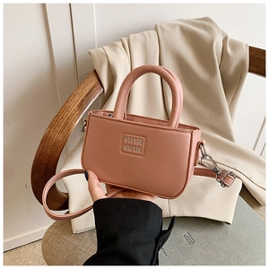 Détail d'un mini sac à main rose avec logo AIR en métal sur veste beige et chaise