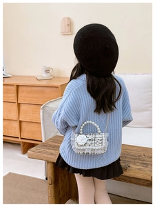 Detailed view of child's tweed bag with white rose, lace trim and pearl handle on model