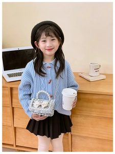 Girl's tweed crossbody bag with white mesh bow and pearl handle in home setting