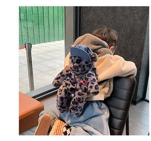 Detail of child wearing a purple leopard plush bear backpack with a blue cap and neckerchief