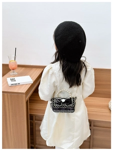 Kid's tweed crossbody bag with black bow and pearl handle shown on a child model