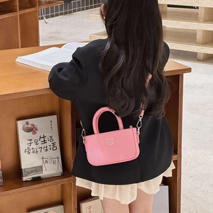 Mini sac à main rose pour enfant en cuir avec bandoulière porté par un mannequin