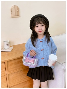 Detailed view of child fashion crossbody bag with pearl handle and bow on knit cardigan