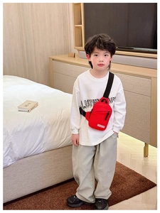 Detailed view of kids red chest bag with adjustable black strap worn by a young boy