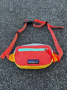 Détail du sac bandoulière enfant en nylon ripstop coloré avec logo de montagne sur asphalte