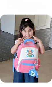 Girl wearing pink cartoon bear backpack with blue handle and circular mini pouch charm