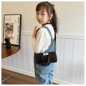 Child wearing a black canvas cylinder crossbody bag with fashion letter patch in a cozy room