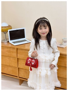 Detail of red sequined girls purse with pearl handle and bow paired with tweed dress