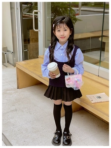 Girl in British school style outfit featuring purple knit vest and pink bow handbag