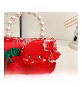 Detail of red satin girls handbag with pearl handle and knit cherry decoration